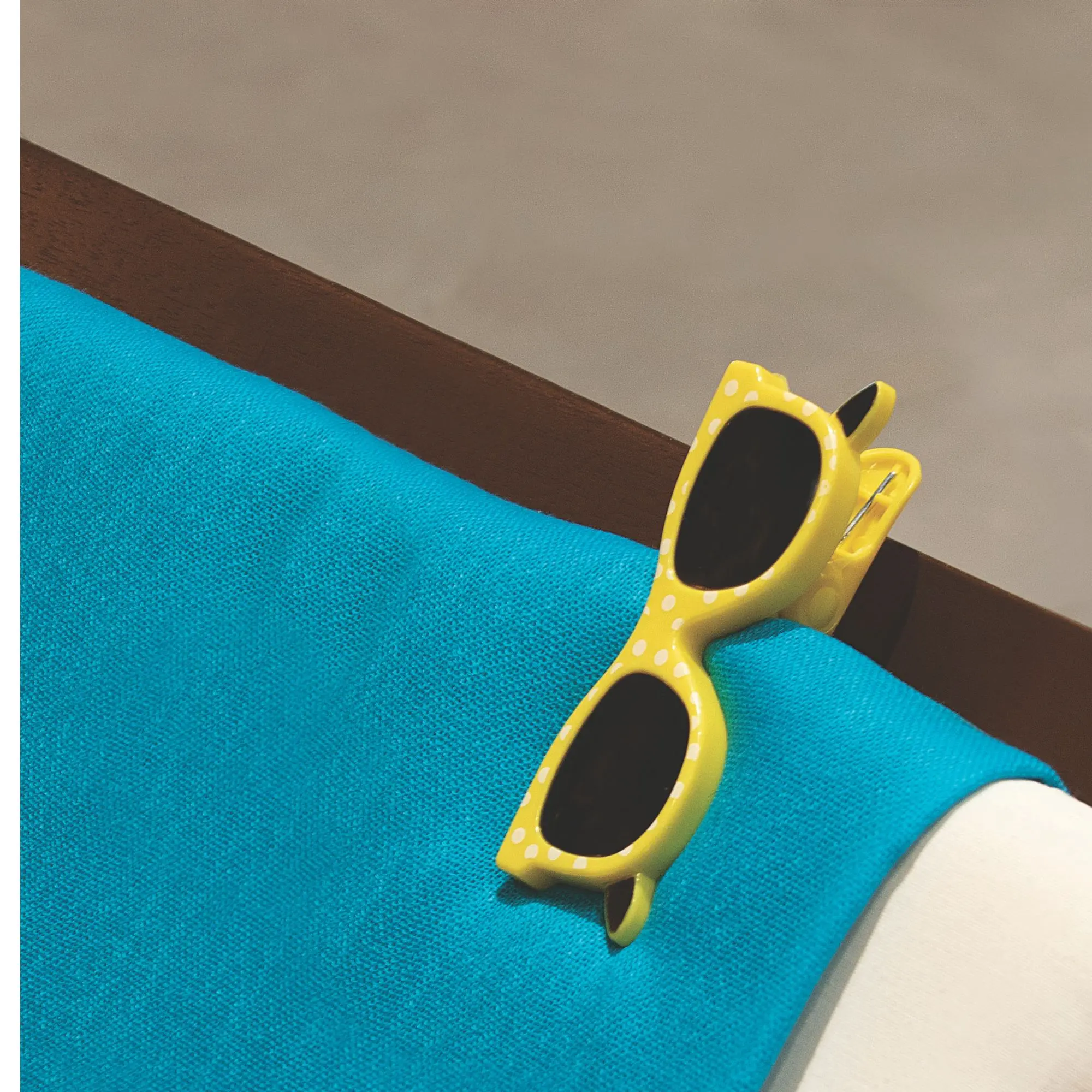 Detalhe aproximado do Clipe Toalha de Praia Óculos Tobee fixado firmemente no encosto de uma cadeira.