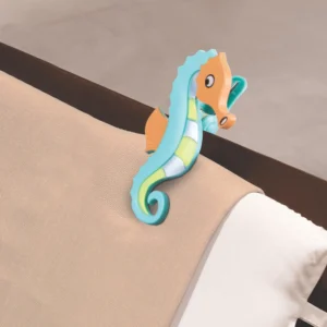 Espreguiçadeira com toalha listrada azul e amarela de frente para o mar azul com o prendedor de cavalo marinho Tobee em destaque.
