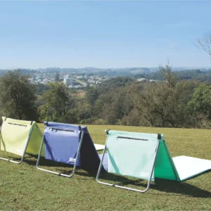 Espreguiçadeiras portáteis dobráveis para camping, praia e lazer, em três cores diferentes sobre gramado ao ar livre.
