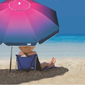 Pessoa sentada em uma cadeira de praia sob a sombra de um guarda-sol azul marinho e rosa Tobee.