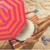 Visão aérea de modelo na espreguiçadeira sob a sombra do Guarda Sol Aruba Tobee listrado vermelho e laranja na areia.