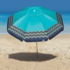 Guarda-sol de praia Tobee na cor azul-turquesa com bordas decoradas em ondas laranjas, aberto na areia fina com o mar ao fundo.