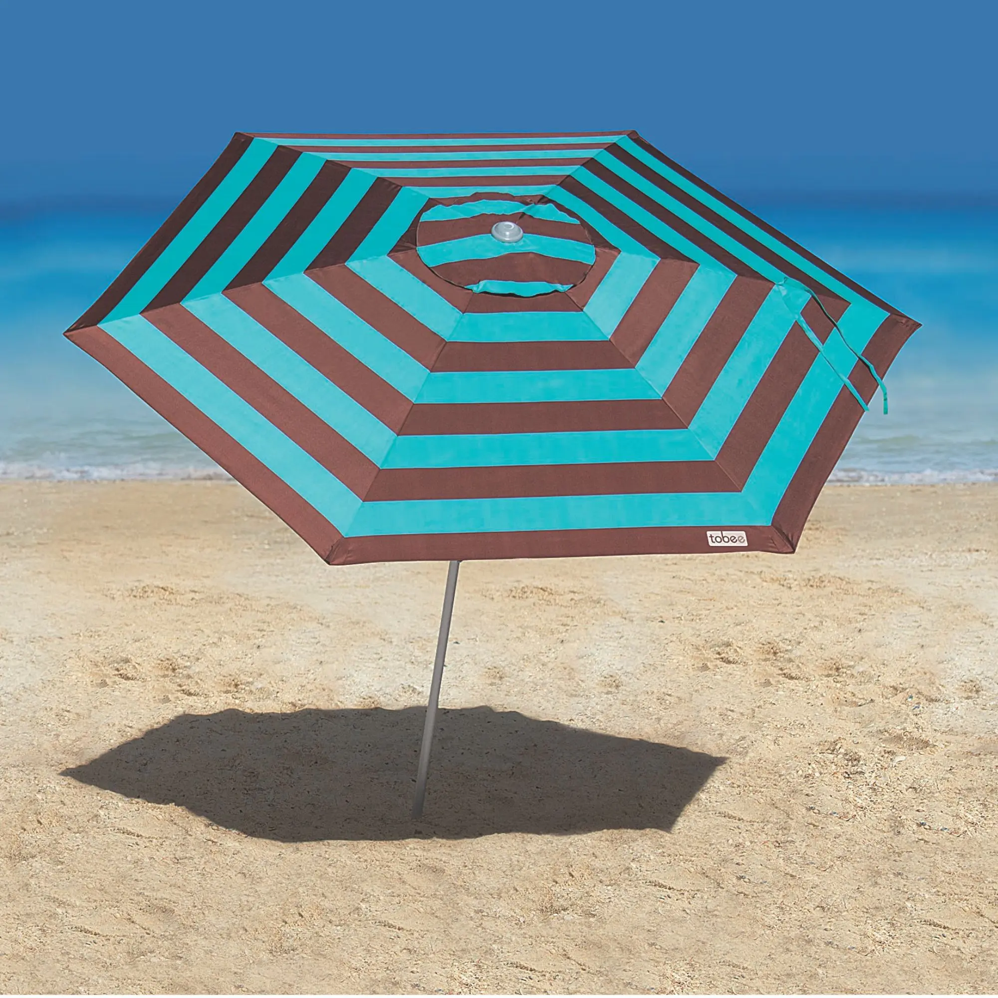 Guarda-sol ombrelone Malibu Tobee fixado na areia da praia com sombra projetada e mar azul ao fundo