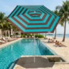 Guarda-sol ombrelone Malibu Tobee em destaque à beira da piscina com uma praia paradisíaca ao fundo.