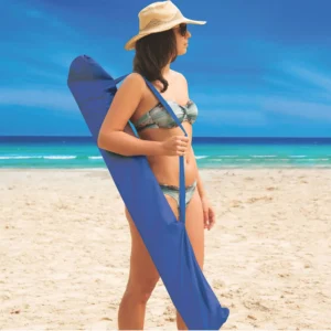 Mulher na praia carregando o guarda-sol Malibu Tobee azul dentro da sacola de transporte com alça.