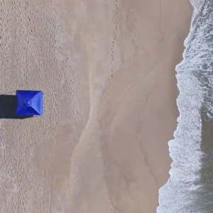 Vista aérea por drone da Tenda Gazebo Tobee na beira do mar, destacando a projeção de sombra da Tenda Gazebo Flex 3 X 3m Dobrável Em Alumínio Uv50+ Tobee na areia.